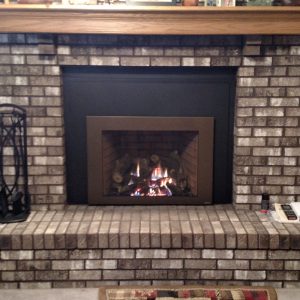 Black fireplace with brass trimings built into a brick mantel